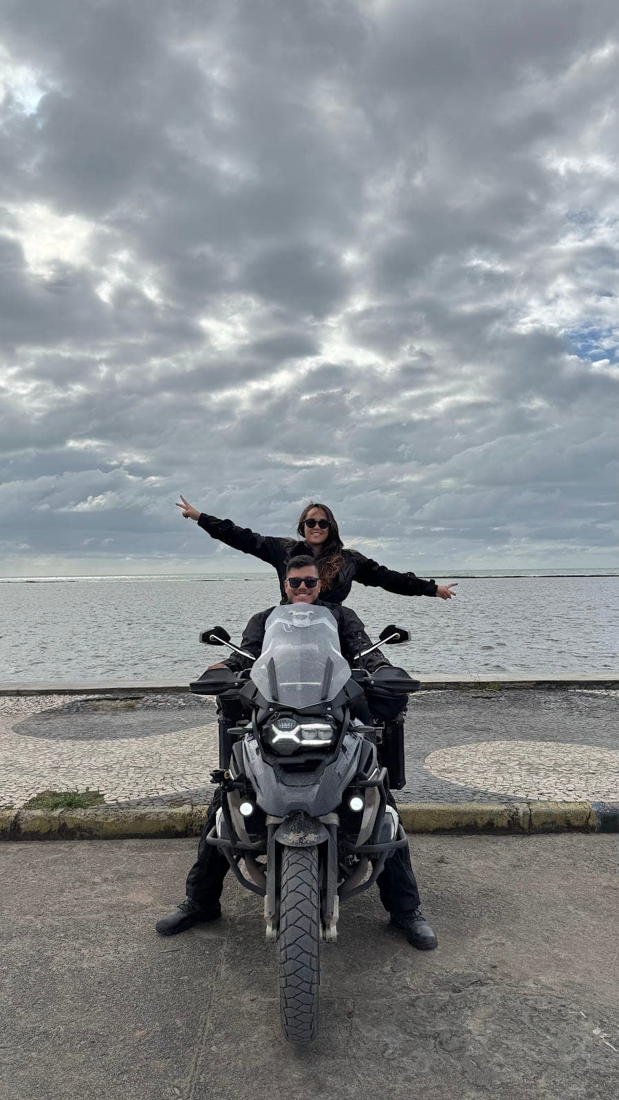 Na moto de frente pro mar, ela em pé no banco
